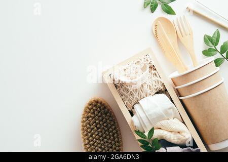 Einweggeschirr, Holzkiste mit Stoffeinkauftaschen, Pinsel, grüne Blätter auf weißem Hintergrund. Umweltfreundliches Besteck, Blick von oben. Nachhaltige Lebensstheit Stockfoto
