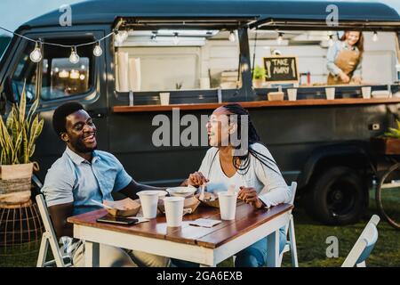 Glückliches schwarzes Paar, das beim Abendessen in der Nähe des Food Trucks lachte Stockfoto