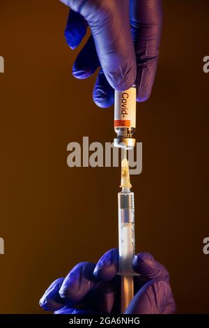 Hand mit blauem Handschuh und Spritze zum Zeichnen des Covid-19-Impfstoffs Stockfoto