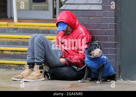 Obdachloser Mann mit verstümmelten Hunden in Preston, Lancashire. Vereinigtes Königreich Wetter 29 Juli 2021. Geschäfte, Shopper & Verkäufe an einem nassen und windigen Tag im Stadtzentrum. Es wird für starke Winde und weiteren Regen gerechnet. Quelle: MediaWorldImages/AlamyLiveNews Stockfoto