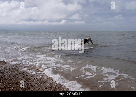 Ein Schwimmer taucht am 25. Juli 2021 in Whitstable, England, in das kalte Gezeitenwasser der Themsemündung ein. Stockfoto