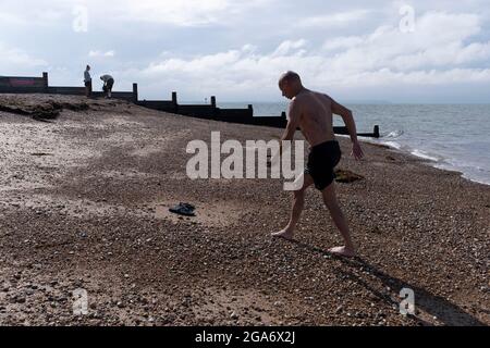 Ein kalter und müder Schwimmer humpelt nach einem Bad im kalten Gezeitenwasser der Themse-Mündung am 25. Juli 2021 in Whitstable, England, über Strandkies. Stockfoto