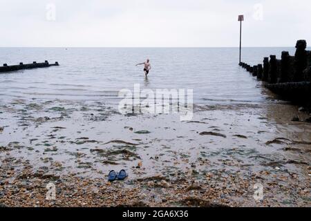 Ein wilder Schwimmer geht auf dem Kiesel zurück zu seinen Schuhen, nachdem er am 26. Juli 2021 in Whitstable, England, im kalten Gezeitenwasser der Themse geschwommen war. Stockfoto