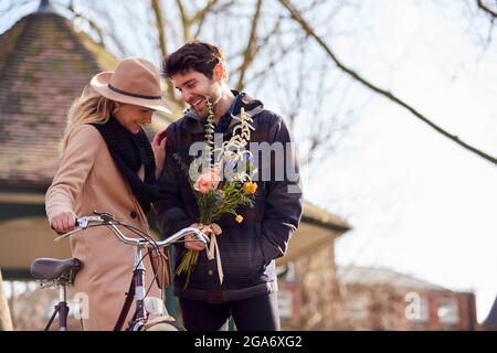 Frau Mit Fahrrad Trifft Mann, Der Blumen Auf Dem Date Im Stadtpark Hält Stockfoto