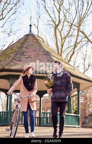 Frau Mit Fahrrad Trifft Mann, Der Blumen Auf Dem Date Im Stadtpark Hält Stockfoto