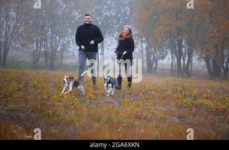 Glückliches junges Familienpaar mit zwei Hunden, die im Herbstpark laufen Stockfoto