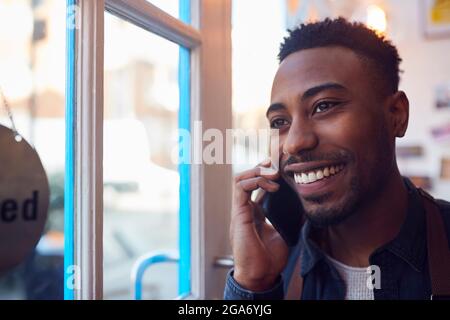 Inhaber Eines Kleinen Unternehmens, Der Am Geschäftstor Steht Und Auf Dem Mobiltelefon Anruft Stockfoto