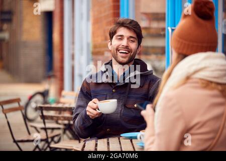 Ein Paar Am Date Sitzt Vor Dem Coffee Shop Auf Der Geschäftigen City High Street Und Schaut Sich Digitale Geräte An Stockfoto