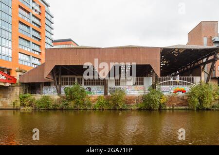 Blick von der Salford-Seite über den Fluss Irwell des Riverside House, einem stillgegangenem Lagerhaus mit Graffiti, Spinningfields, Manchester, Nordwestengland Stockfoto