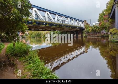 Eiserne Fußgängerbrücke, die das Ufer des Flusses Irwell, Salford und Castlefield, Manchester, im Nordwesten Englands, überspannt, mit Spiegelungen und Treidelpfaden Stockfoto