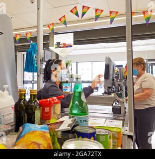 Junge Arbeiterin mit covid facemask im Co Op Supermarkt, die an der Kasse für Lebensmittel bei einer Pandemie arbeitete Großbritannien, Großbritannien, KATHY DEWITT Stockfoto