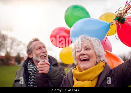 Liebende Senioren Halten Ballons Genießen Herbst Oder Winter Spaziergang Durch Park Zusammen Stockfoto