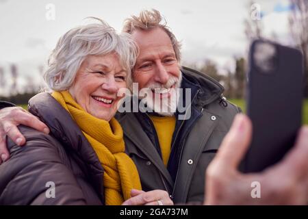 Liebevolles Senior-Paar Posiert Für Selfie Auf Dem Handy Auf Herbst- Oder Winterspaziergang Durch Den Park Stockfoto