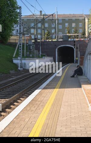 Königsberg, Russland - 11. Mai 2021: Der Mann sitzt auf einer Holztreppe und wartet auf die Ankunft des Zuges Stockfoto