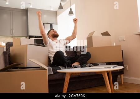 Junger Mann sitzt auf dem Sofa und freut sich zu Hause Stockfoto