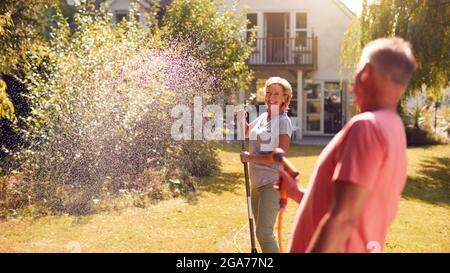 Rentnerpaar Bei Der Arbeit Bewässerung Von Pflanzen Mit Schlauch Und Aufräumen Garten Mit Rake Zu Hause Stockfoto