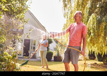 Rentnerpaar Bei Der Arbeit Bewässerung Von Pflanzen Mit Schlauch Und Aufräumen Garten Mit Rake Zu Hause Stockfoto