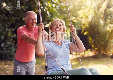 Rentnerpaar Mit Spaß Mit Mann Schieben Frau Auf Garten Schaukel Stockfoto