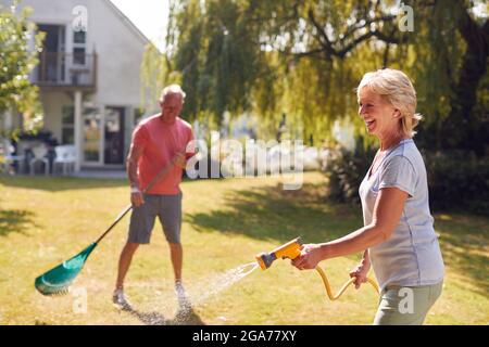 Rentnerpaar Bei Der Arbeit Bewässerung Von Pflanzen Mit Schlauch Und Aufräumen Garten Mit Rake Zu Hause Stockfoto