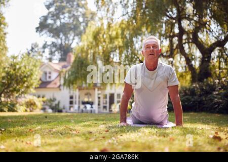 Senior Man Zu Hause Im Garten Trägt Fitness-Kleidung Sitzen Yoga-Übungen Auf Matte Stockfoto