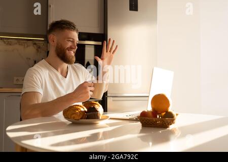 Mann winkt Hand zum Laptop und trinkt Tee Stockfoto
