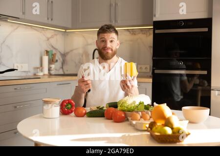 Besorgter Mann sitzt am Tisch und hält Pfeffer und Messer Stockfoto