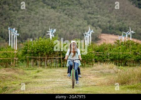 Frau, die Fahrrad auf dem Feld mit Windturbinen im Hintergrund reitet Stockfoto