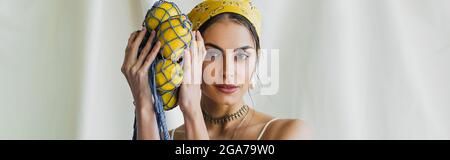 Frau in gelbem Kopftuch mit String-Tasche mit Zitronen auf weißem Banner Stockfoto
