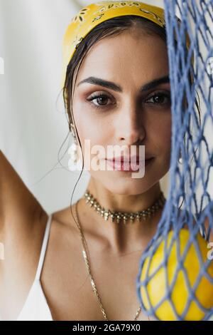 Hübsche Frau in gelbem Kopftuch mit verschwommenem Saitenbeutel mit Zitronen auf Weiß Stockfoto