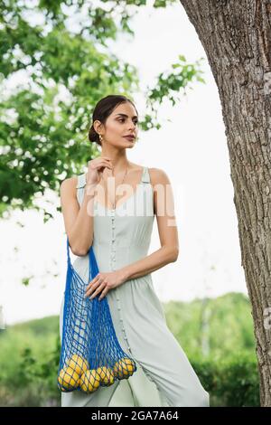 Hübsche Frau, die im Park einen wiederverwendbaren Saitenbeutel mit Zitronen hält Stockfoto