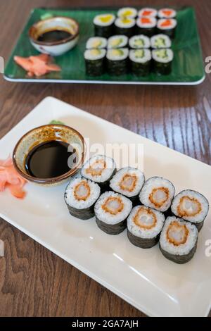 Ein Tisch mit ebi-Fry (gebratene Garnelen) Maki-Sushi und ein Teller mit vegetarischem Sushi, Seitenansicht, vertikal Stockfoto