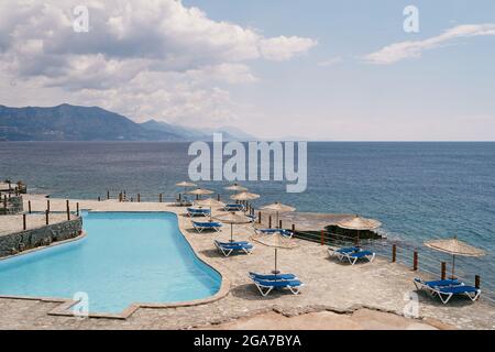 Liegestühle und Sonnenschirme stehen in der Nähe des Pools an einem gepflasterten Strand Stockfoto