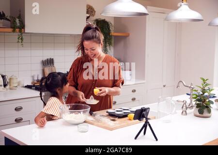 Asiatische Mutter Und Tochter Backen Cupcakes In Der Küche Zu Hause, Während Auf Vlogging Auf Handy Stockfoto
