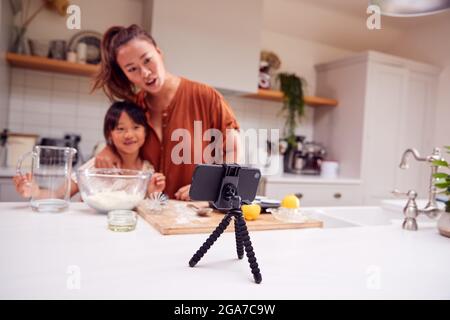 Asiatische Mutter Und Tochter Backen Cupcakes In Der Küche Zu Hause, Während Auf Vlogging Auf Handy Stockfoto