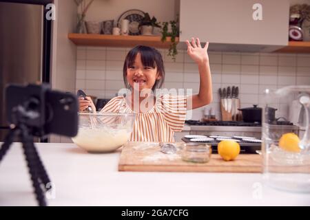 Asiatische Mädchen Backen Cupcakes In Der Küche Zu Hause, Während Auf Vlogging Auf Handy Stockfoto