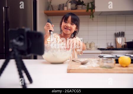 Asiatische Mädchen Backen Cupcakes In Der Küche Zu Hause, Während Auf Vlogging Auf Handy Stockfoto