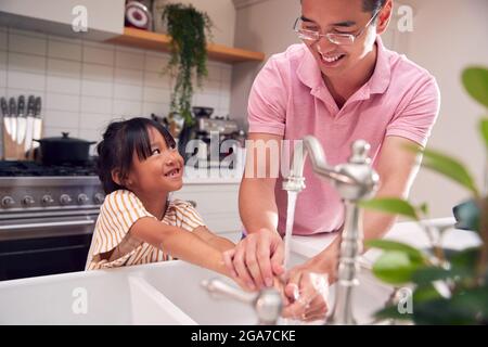 Asiatischer Vater Hilft Tochter, Sich Zu Hause Mit Seife Die Hände Zu Waschen, Um Die Infektion Bei Der Gesundheitspandemie Zu Stoppen Stockfoto