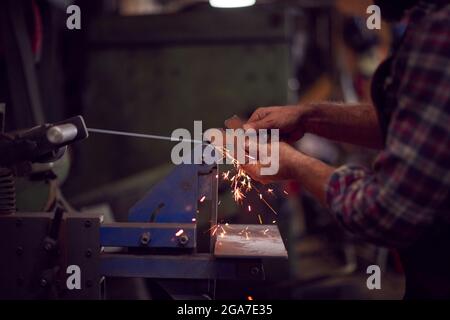 Nahaufnahme Des Schmieds, Der Metallarbeiten Am Belt Sander Mit Sparks Formt Stockfoto