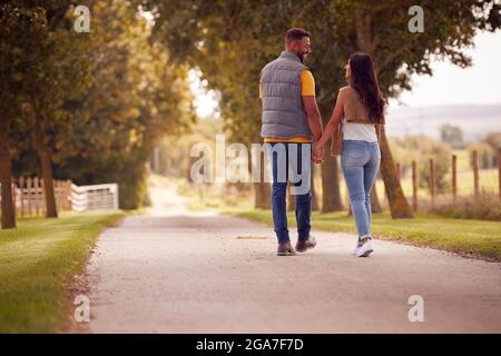 Rückansicht Eines Liebenden Paares, Das Hand In Hand Entlang Des Tracks Durch Die Landschaft Geht Stockfoto