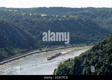 Loreley, Deutschland - 25. Juli 2021. Ein großer Lastkahn, der viele Container auf dem Rhein in Westdeutschland transportiert, sichtbare, von Bäumen bewachsene Hügel. Stockfoto