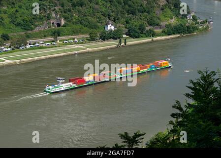 Loreley, Deutschland - 25. Juli 2021. Ein großer Lastkahn, der viele Container auf dem Rhein in Westdeutschland transportiert, sichtbare, von Bäumen bewachsene Hügel. Stockfoto