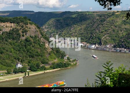 Loreley, Deutschland - 25. Juli 2021. Ein großer Lastkahn, der viele Container auf dem Rhein in Westdeutschland transportiert, sichtbare, von Bäumen bewachsene Hügel. Stockfoto