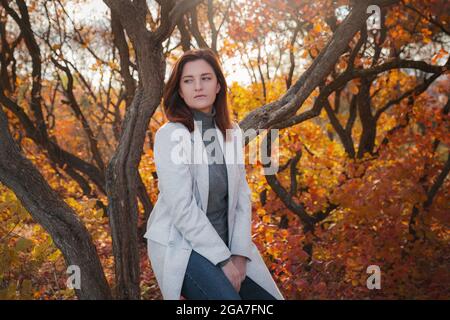 Eine niedliche rothaarige Frau in guter Laune posiert an einem Herbsttag und genießt das schöne Wetter. Das Konzept und die Idee, Herbst und Herbst Getaway zu genießen Stockfoto