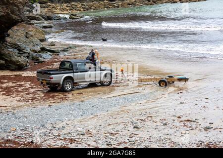 Trevaunance Cove, Großbritannien, 29. Juli 2021,EIN Mann kehrt in einem kleinen Holzboot an Land zurück, das er dann auf einen Anhänger am Strand verladen hat. Es gab Wellen in Trevaunance Cove vor dem Sturm Evert in St. Agnes, Cornwall. Der vierte genannte Sommersturm wird über Nacht für unSaison starke Winde und starken Regen sorgen.Quelle: Keith Larby/Alamy Live News Stockfoto