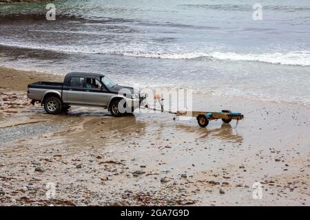 Trevaunance Cove, Großbritannien, 29. Juli 2021,EIN Mann kehrt in einem kleinen Holzboot an Land zurück, das er dann auf einen Anhänger am Strand verladen hat. Es gab Wellen in Trevaunance Cove vor dem Sturm Evert in St. Agnes, Cornwall. Der vierte genannte Sommersturm wird über Nacht für unSaison starke Winde und starken Regen sorgen.Quelle: Keith Larby/Alamy Live News Stockfoto