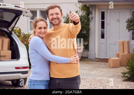 Porträt Eines Paares, Das Schlüssel Vor Dem Neuen Zuhause Hält Am Umzugstag Entladen Von Kisten Aus Dem Auto Stockfoto