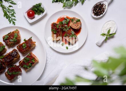Flach mit gefüllten Kohlrollen in Tomatensauce, Petersilie und wenigen Zutaten auf weißen Tellern, einschließlich saurer Rahm und Pfeffer, legen. Unfokussierte Petersilie A Stockfoto