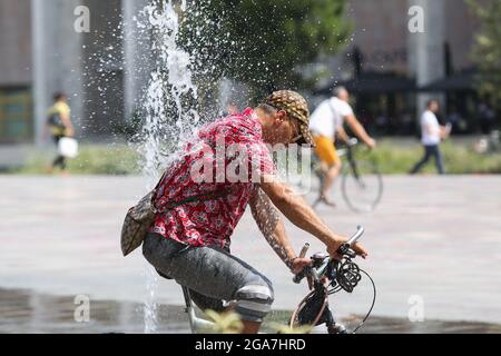 (210729) -- TIRANA, 29. Juli 2021 (Xinhua) -- EIN Mann fährt mit dem Fahrrad durch Brunnen auf dem Skanderbeg-Platz im Zentrum der Hauptstadt Tirana, Albanien, 29. Juli 2021. Die Temperatur in Tirana erreichte am Donnerstag 40 Grad Celsius. (Foto von Gent Onuzi/Xinhua) Stockfoto