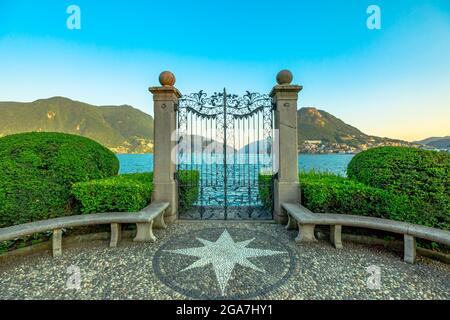 Tor am Luganer See im öffentlichen Ciani Park der Schweiz. Der Seeufer der Stadt Lugano im Kanton Tessin. Parkbank mit Windrose aus Steinen Stockfoto