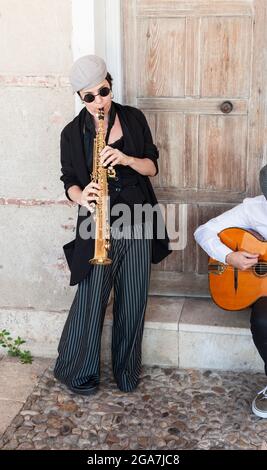 Jazzmusiker im Retro-Stil spielen auf der Straße. Eine brünette Frau, die mit Kappe und Sonnenbrille auf Klarinette steht und im f nach vorne blickt Stockfoto